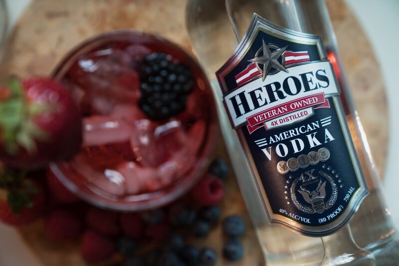 A bottle of Heroes Vodka is showcased above a berry cocktail